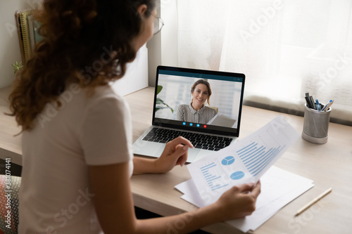 Businesswoman talk speak brainstorm on video call from home, discuss company financial document at online meeting. Female employee have webcam virtual digital conference with woman boss or director.