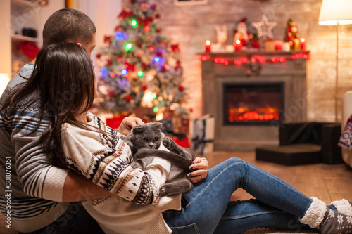 Romantic couple with scottish fold enjoying christmas in front of warm fireplace.