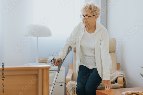 Quadro su tela Old lady with a cane gets up from a chair from a room in a retirement home