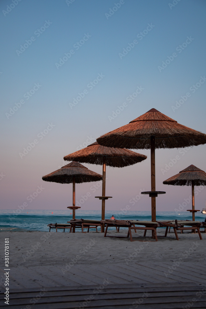 Beautiful dusk and blue hour light just after sunset in a beach club in Villasimius, Sardinia, italy. Straw sub umbrellas and wooden sunbeds, soft pink sky, summer magic atmoshpere.
