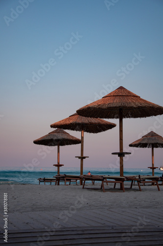 Beautiful dusk and blue hour light just after sunset in a beach club in Villasimius  Sardinia  italy. Straw sub umbrellas and wooden sunbeds  soft pink sky  summer magic atmoshpere.