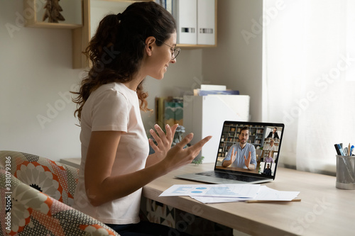 Smiling young female employee at home speak talk on video call on laptop with diverse colleagues. Millennial woman worker have webcam conference or digital web team meeting or briefing with coworkers. photo