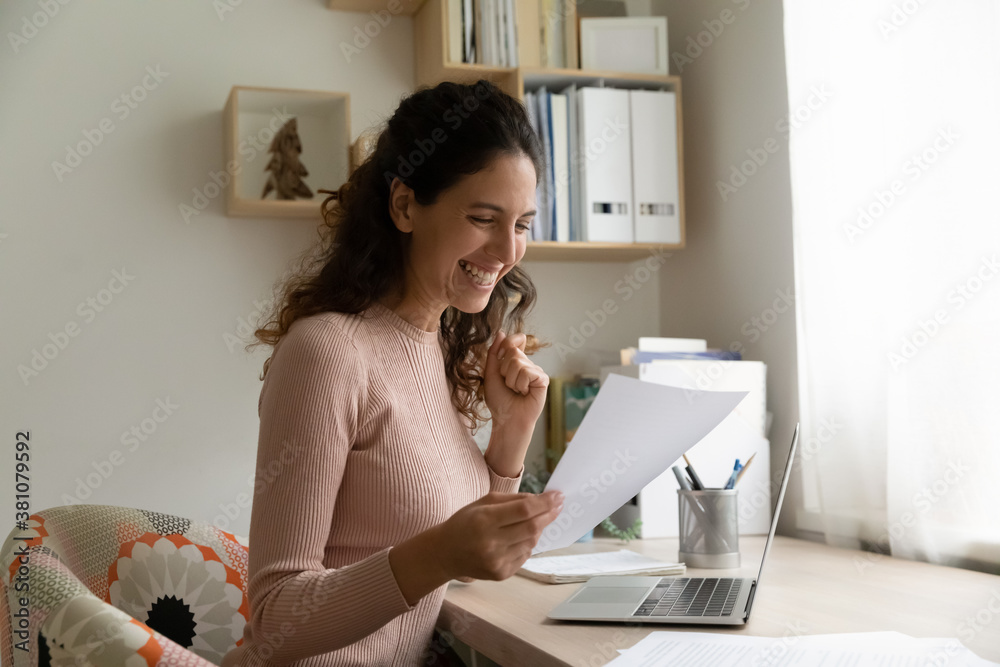 Overjoyed millennial Caucasian woman work on laptop at home triumph reading good news in paperwork letter. Excited young female feel euphoric by pleasant message notice in paper post correspondence. Overjoyed millennial Caucasian woman work on laptop at home triumph reading good news in paperwork letter. Excited young female feel euphoric by pleasant message notice in paper post correspondence.