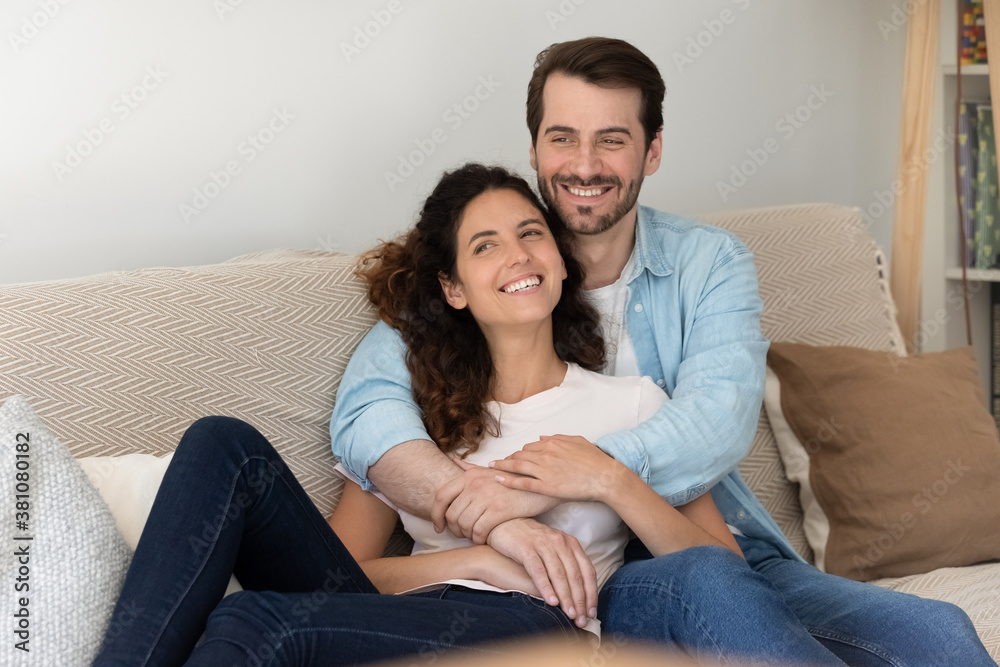 Overjoyed young Caucasian couple tenants relax on couch at home hugging look in distance dreaming visualizing. Happy renters rest on sofa embrace, enjoy family weekend in new house. Realty concept. Overjoyed young Caucasian couple tenants relax on couch at home hugging look in distance dreaming visualizing. Happy renters rest on sofa embrace, enjoy family weekend in new house. Realty concept.