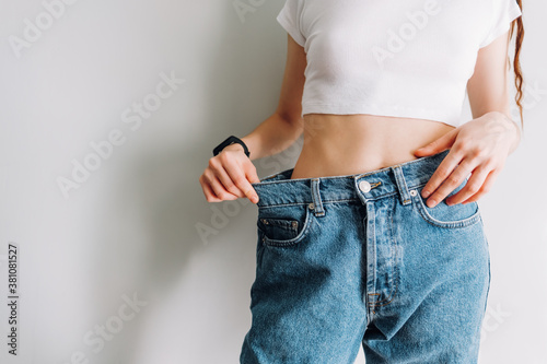 Slimming concept. Young woman holds jeans in her hand, shows a thin waist Slim female body in large jeans. Successful weight loss.