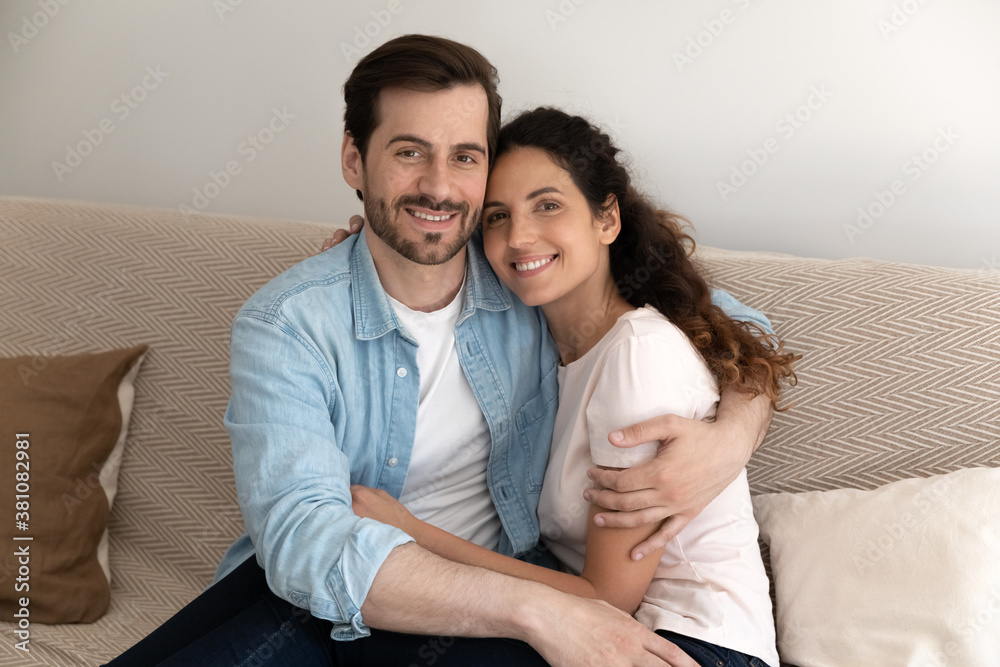 Portrait of happy young Caucasian couple tenants sit on sofa in new home, excited moving together. Smiling renters hug embrace relax on couch in own house. Real estate, realty, relocation concept. Portrait of happy young Caucasian couple tenants sit on sofa in new home, excited moving together. Smiling renters hug embrace relax on couch in own house. Real estate, realty, relocation concept.
