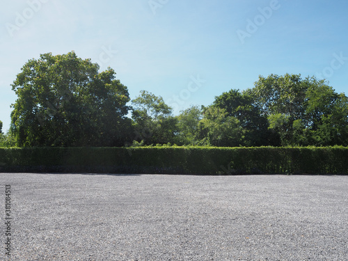 Parking lot sprinkled with gravel bush green tree blue sky nature background