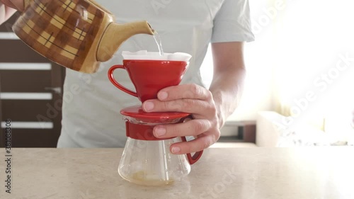 Homemade coffee. Pourover. A man brews at home v 60. He pours hot water into a red ceramic dripper with a filter and coffee drips into a glass server