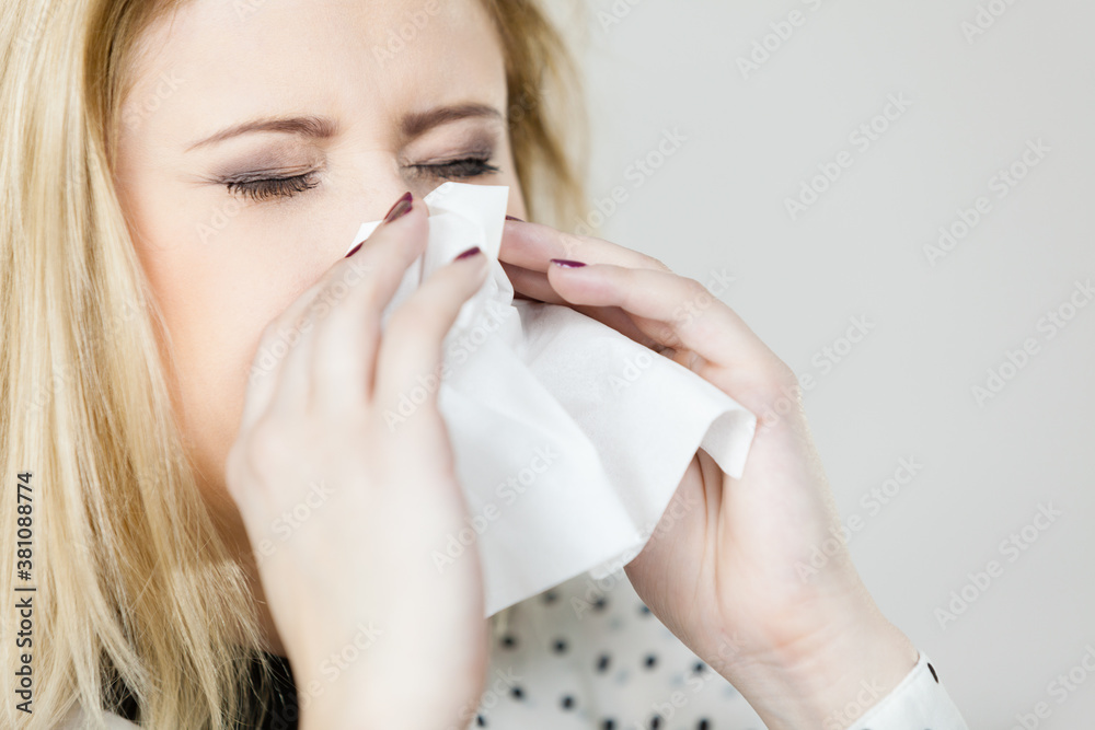 Woman being sick having flu sneeze into tissue Woman being sick having flu sneeze into tissue