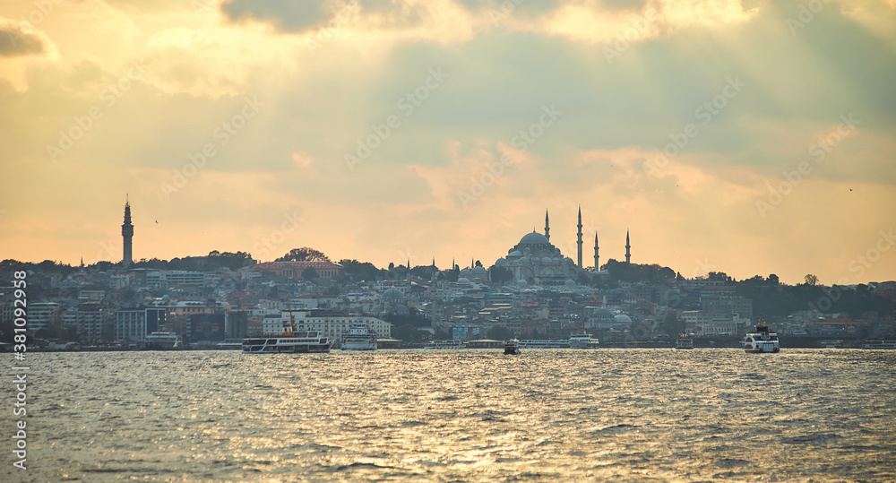 Sunset over Istanbul with a view of the Suleymaniye  Mosque and City line ferry and boats. Traditional arabic town with silhouettes of minarets on sunset, ancient landmarks of architecture in Turkey.