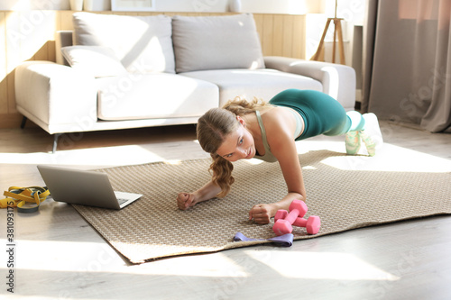 Fitness woman doing plank and watching online tutorials on laptop, training in living room. Stay at home activities. Top view.