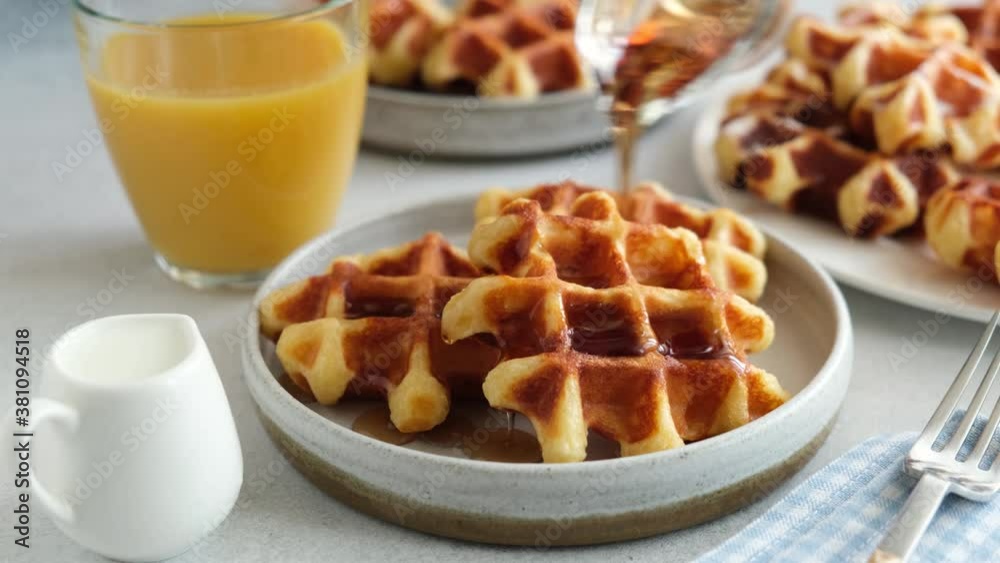 Pouring maple syrup on belgian waffles. Tasty breakfast waffles with sweet syrup and golden belgian waffles Pouring maple syrup on belgian waffles. Tasty breakfast waffles with sweet syrup and golden belgian waffles