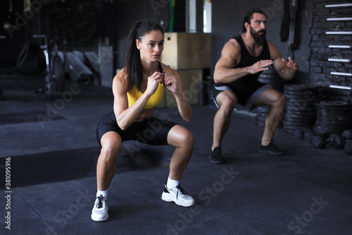 Fitness couple in sportswear doing squat exercises at gym.