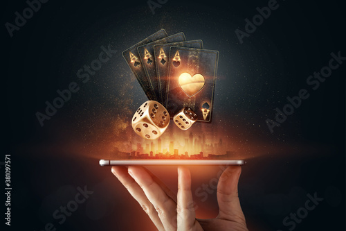 Photography Creative background, online casino, in a man's hand a smartphone with playing cards, roulette and chips, black-gold background