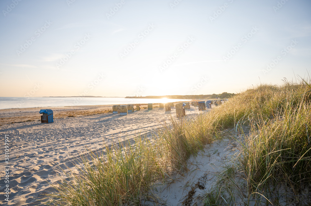 beach chairs stand on a baltic sea beach in the light of the rising sun with the sea in the background in the foreground thin grass is flooded with light beach chairs stand on a baltic sea beach in the light of the rising sun with the sea in the background in the foreground thin grass is flooded with light