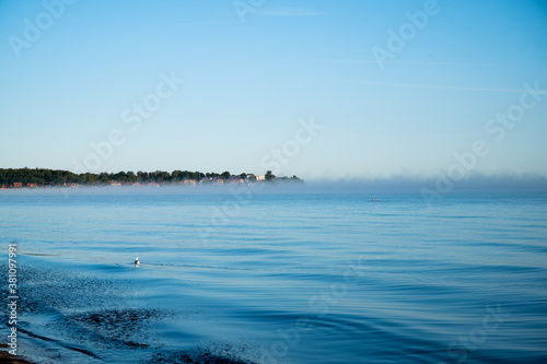 ocean with light waves in bright blue as conceptual background with a horizon shrouded in light fog and a city in the background with lots of space for text or design