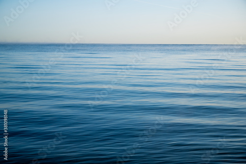 ocean with light waves in bright blue as conceptual background with horizon and a lot of space for text or design