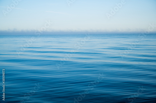 ocean with light waves in bright blue as conceptual background with horizon and a lot of space for text or design