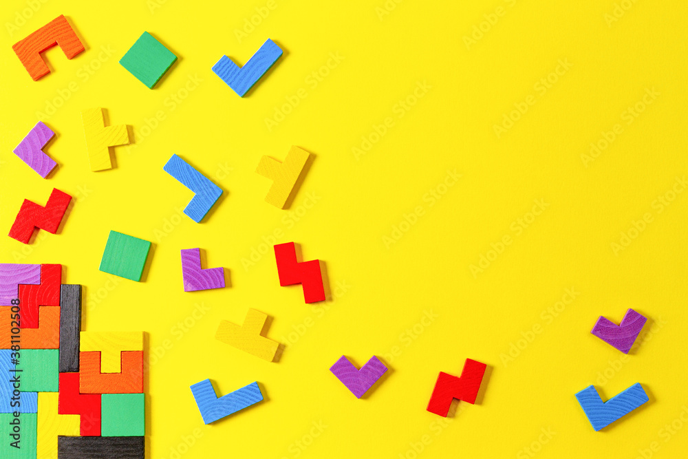 Different colorful shapes wooden puzzle blocks on yellow background. Geometric shapes in different colors, top view Different colorful shapes wooden puzzle blocks on yellow background. Geometric shapes in different colors, top view