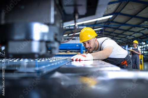 Factory worker in protective uniform and hardhat operating industrial machine at production line. People working in industry.