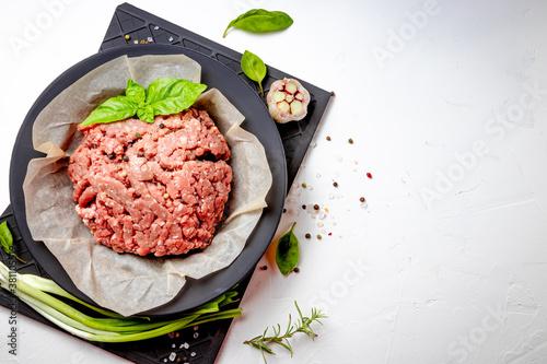  Minced meat in a plate and spices on a black background, top view, free space for your text