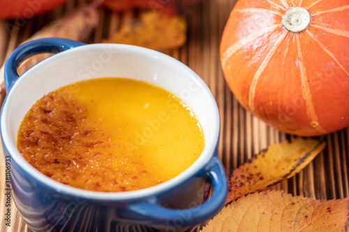 orange Creme Brulee aus Kürbis vom Hokkaido mit karamellisierter Zuckerkruste in Förmchen auf einem braunen Holztisch mit Laubblättern im Herbst