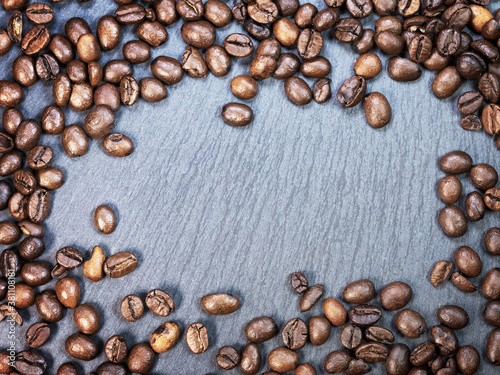 Texture of scattered roasted coffee beans on a gray graphite background. Bright abstract background ideal for any design