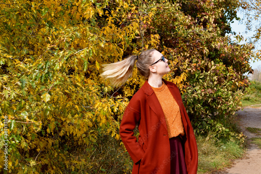 Young woman with blond hair made up in a ponytail in the autumn park on a sunny day. Embracing the new season