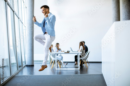 Young businessman with smartphone jumping in a modern office