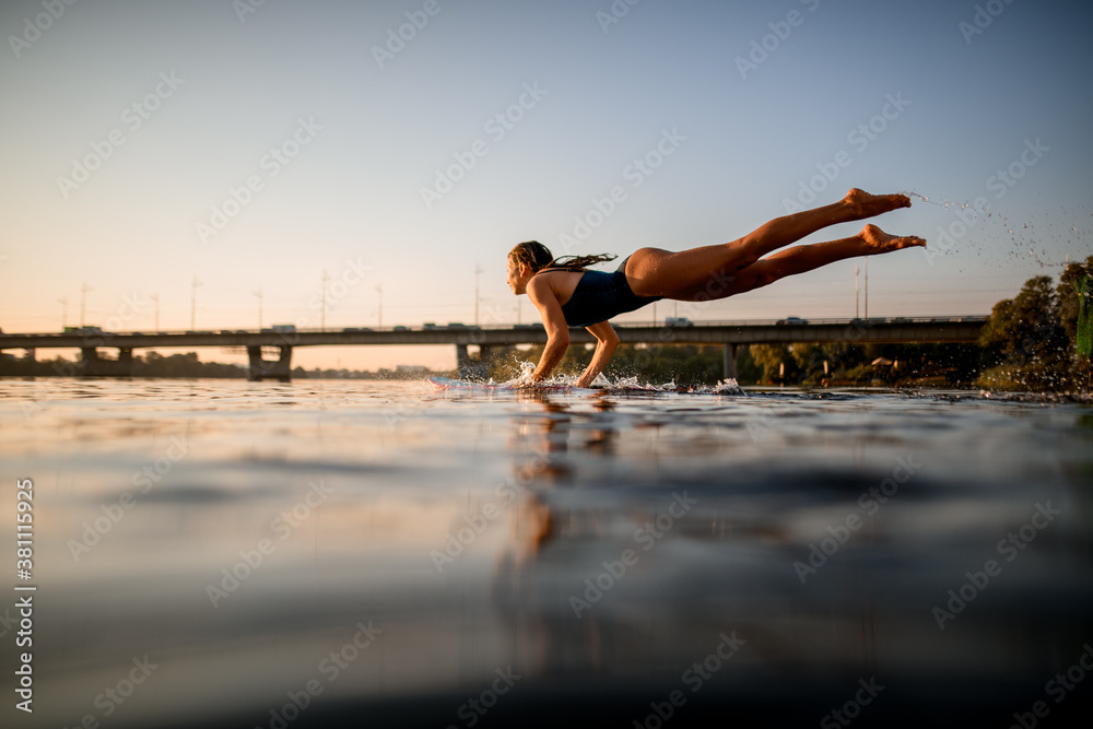 view of woman with surf style wakeboard in her hands flies over the water