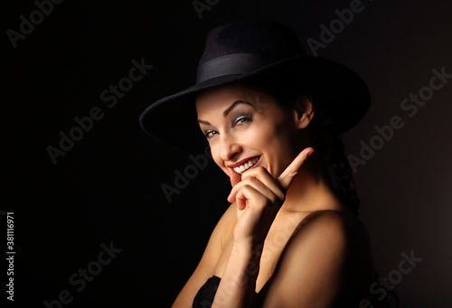 Beautiful excited positive young woman in style blue hat smiling and hava an good idea showing and conjuresing the finger sign on dark shadow background. Closeup portrait. Halloween concept. photo