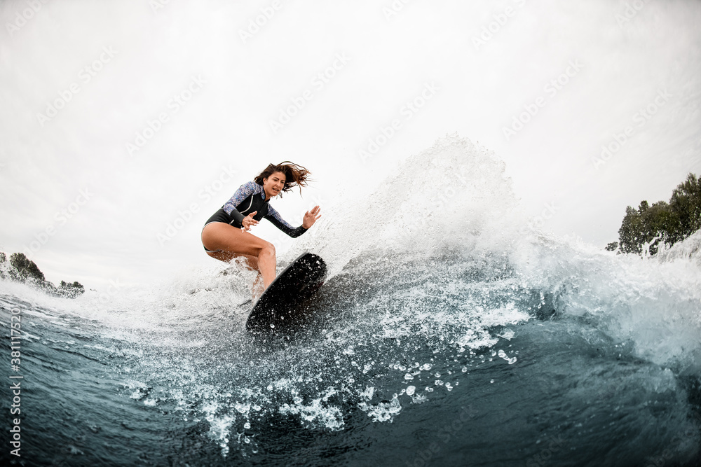 View of woman in swimsuit who engaged in extreme sport and rides board on river wave