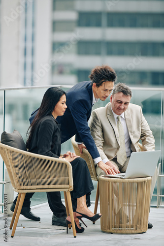 Multi-ethnic business people reading report on laptop whne having meeting on rooftop photo