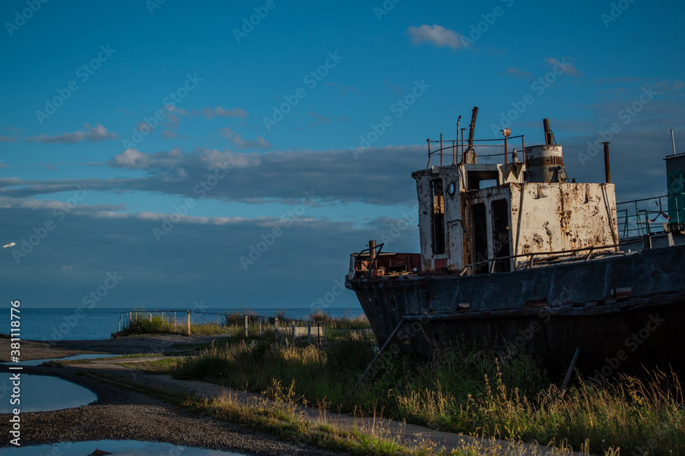 old rusty ship, boat on grassy shore in light of sunset, near puddles. White vessel on coast of lake Baikal, blue sky old rusty ship, boat on grassy shore in light of sunset, near puddles. White vessel on coast of lake Baikal, blue sky