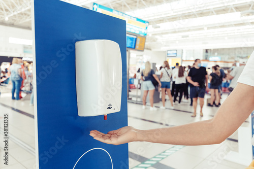 A female passenger disinfects her hands with an automatic sanitizer dispenser in the airport. Health care and protection from infection during the coronavirus pandemic photo