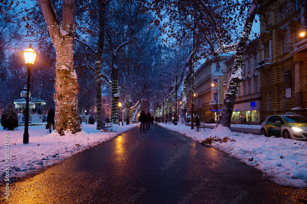 Footpath with decorated trees in Zrinjevac Park in Zagreb at night in winter with snow, Croatia