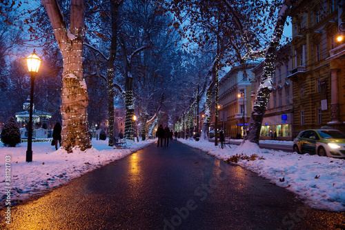 Footpath with decorated trees in Zrinjevac Park in Zagreb at night in winter with snow, Croatia