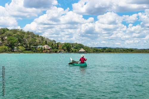Fisherman in canoe boat in lake Itza rowing towards village with sunny cloud sky  El Remate  Peten  Guatemala