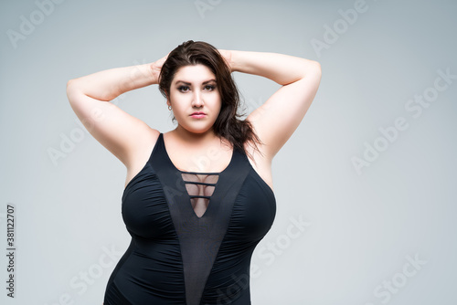Sexy plus size fashion model in black one-piece swimsuit, fat woman in lingerie on gray background