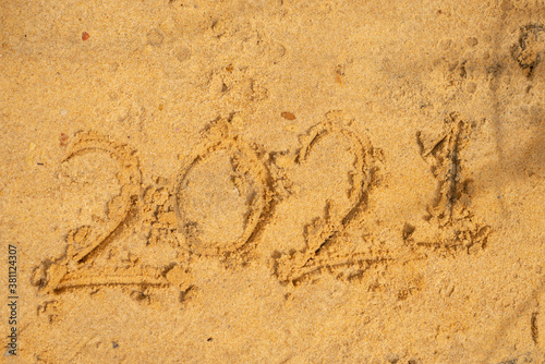 Photo of wave washing out 2021 numbers written on wet sand at beach. Concept of New Year, Christmas and travel on winter holidays.