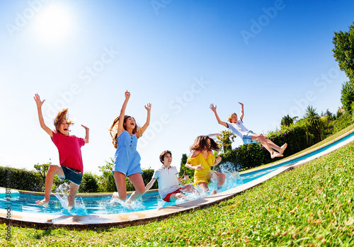Happy laughing group of kids fall and splash into the pool water low angle view over blue sky © Sergey Novikov