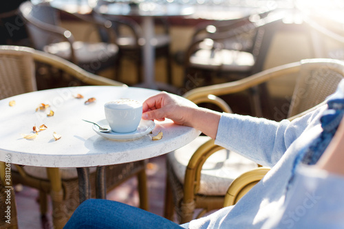 Senior woman drinking coffee in autumn cafe. Retired person relaxation and enjoying morning sun outdoors. Cozy street restaurant with fallen leaves on table. Close up of female hands with cup.