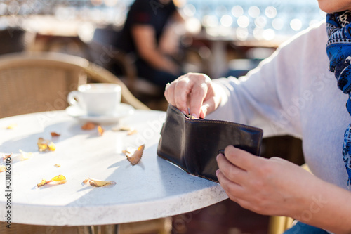 Senior woman pays money in autumn cafe outdoors. Payment for coffee in restaurant. Retired lady holding wallet with cash. Close up of female hands.