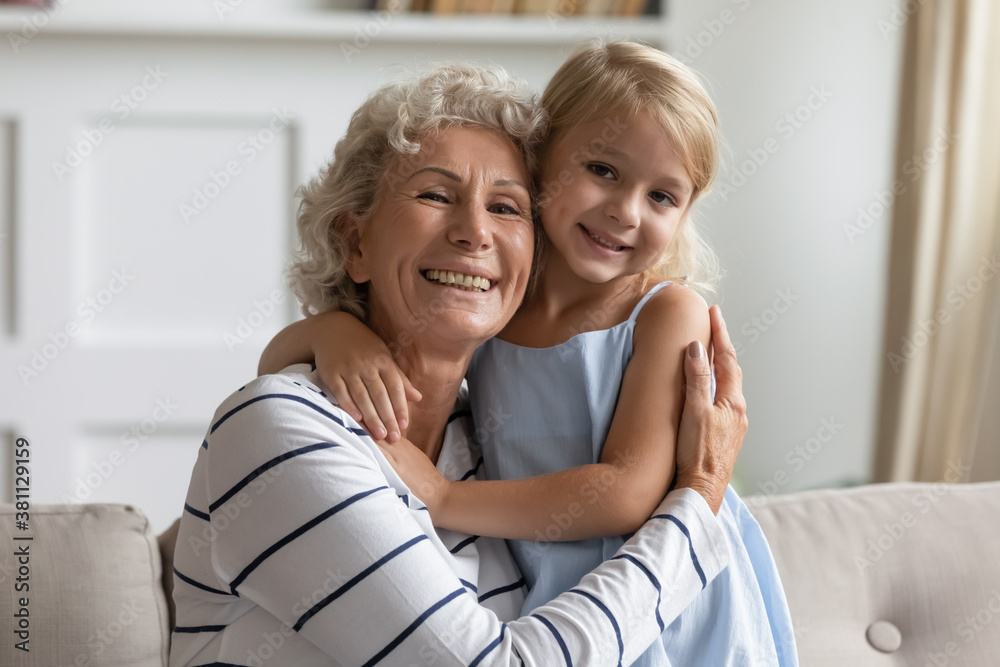 My beloved little girl. Happy caring aged grandmother tender holding smiling preschool granddaughter in arms, lovely small kid cuddling together with senior silver-haired granny on sofa at living room My beloved little girl. Happy caring aged grandmother tender holding smiling preschool granddaughter in arms, lovely small kid cuddling together with senior silver-haired granny on sofa at living room