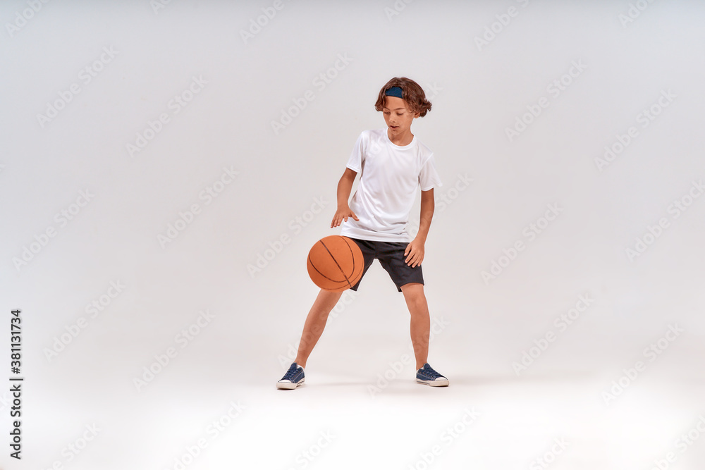 Competition. Full-length shot of a teenage boy playing basketball while standing isolated over grey background Competition. Full-length shot of a teenage boy playing basketball while standing isolated over grey background