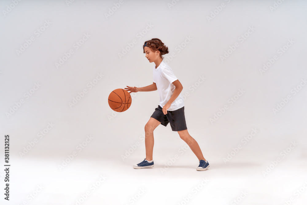 Little winner. Full-length shot of a teenage boy playing basketball while standing isolated over grey background, studio shot