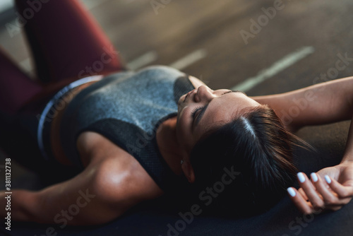 Young exhausted caucasian woman in sportswear lying on the floor at gym and resting after workout, taking a break
