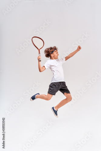 Full-length shot of a teenage boy jumping with a tennis racket isolated over grey background, studio shot © Kostiantyn