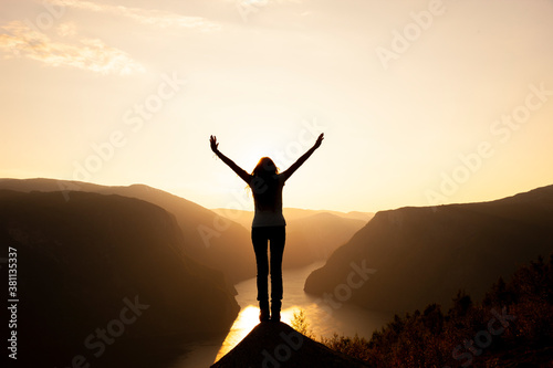 Silhouette einer Frau mit ausgebreiteten Armen bei Sonnenaufgang  auf einem B...