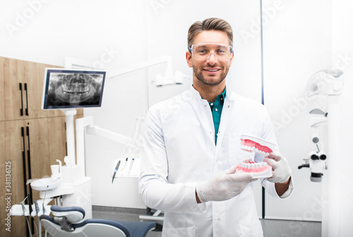 Confident male dentist standing in his modern clinic. Dental hygienist wearing protective glasses smiling at the camera photo